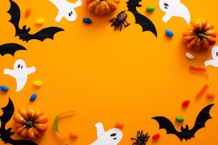 Happy halloween holiday concept. Halloween decorations, pumpkins, bats, candy, ghosts, bugs on orange background. Halloween party greeting card mockup with copy space. Flat lay, top view, overhead.