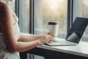 Giovane donna d'affari che utilizza il computer portatile mentre è seduta al tavolo del caffè accanto alle finestre dell'ufficio.