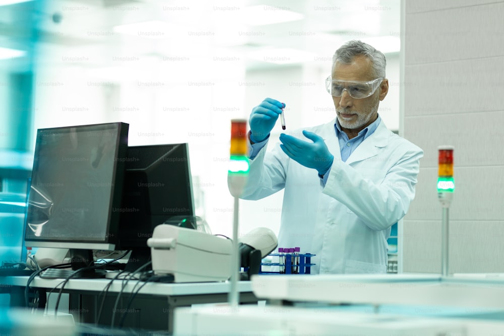 Reagents examination. Serious grey-haired researcher being in lab coat while examining reagent