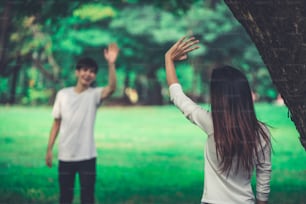 Jóvenes, hombre y mujer saludando o despidiéndose agitando las manos en el parque.