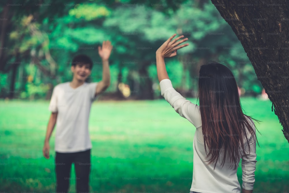 Young people, man and woman greeting or saying goodbye by waving hands in the park.