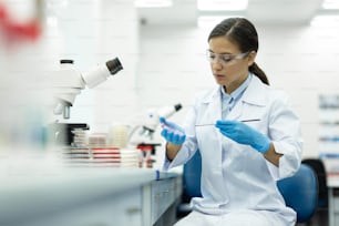 Chemical research. Cheerful brunette girl wearing medical uniform while working with reagent