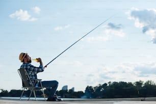 Fishing in summer. Bearded dark-haired man drinking beer and catching fish in summer