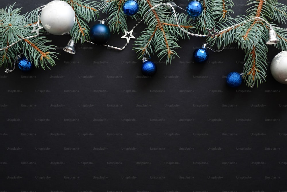 Christmas frame border with blue and sliver modern decorations, baubles, fir tree branches on dark black background. Elegant Christmas banner mockup, greeting card template. Xmas, New Year concept.