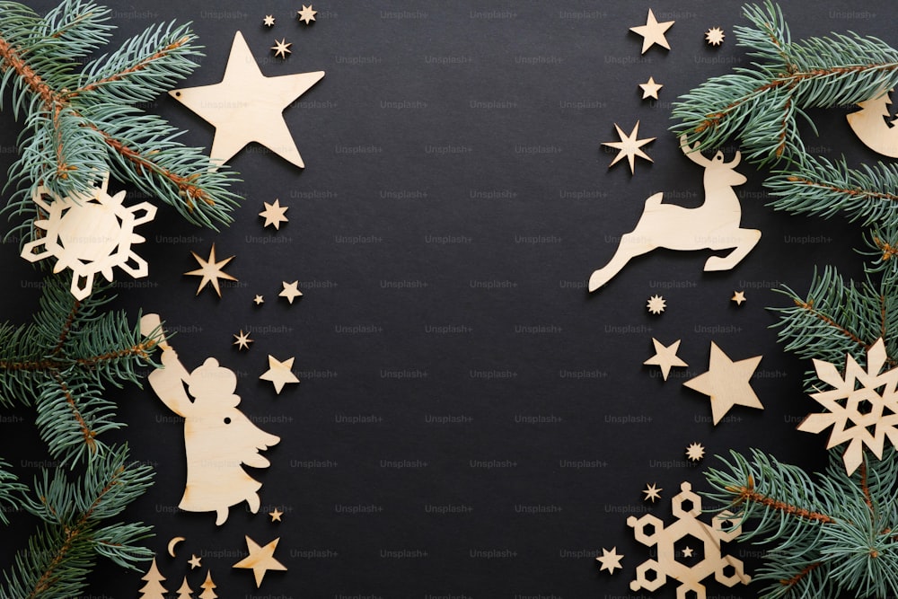 Black Christmas background with handmade wooden decorations and fir tree branches. Christmas holiday celebration, winter, New Year concept. Christmas banner mockup, greeting card template.