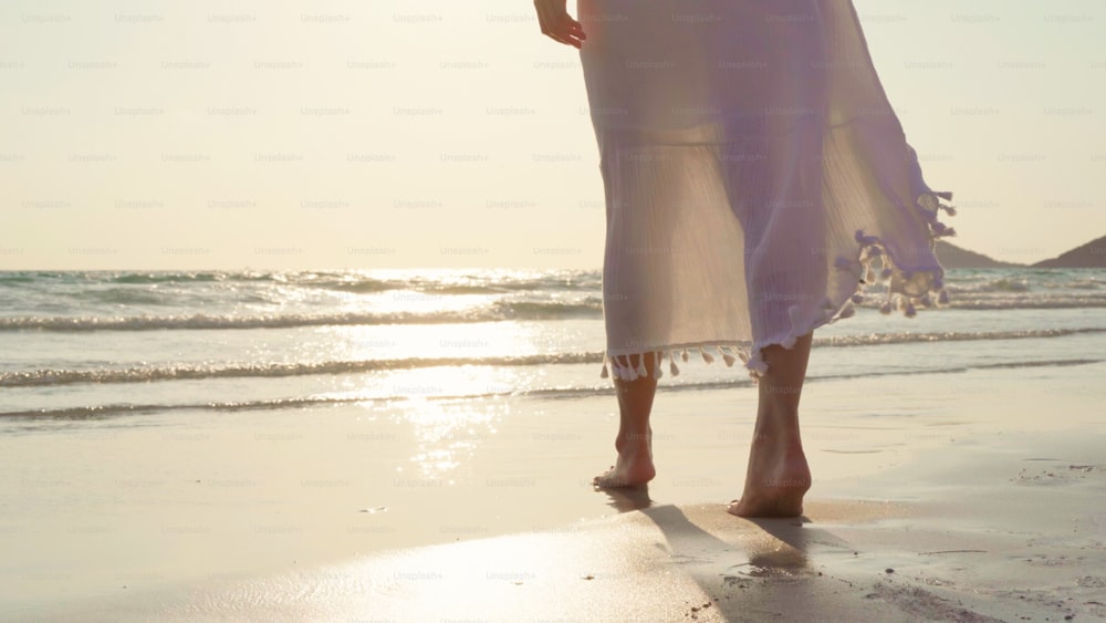 해변을 걷고 있는 젊은 아시아 여성. 아름다운 여성은 저녁에 일몰 때 바다 근처 해변을 산책하며 휴식을 취합니다. 라이프 스타일 여성은 해변 개념으로 여행합니다.