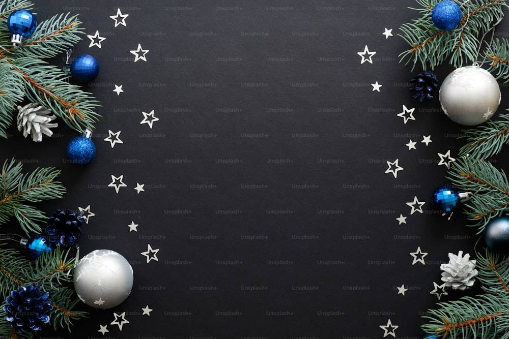 Christmas frame border with blue and sliver modern decorations, baubles, fir tree branches, confetti on dark black background. Elegant Christmas banner mockup, greeting card template