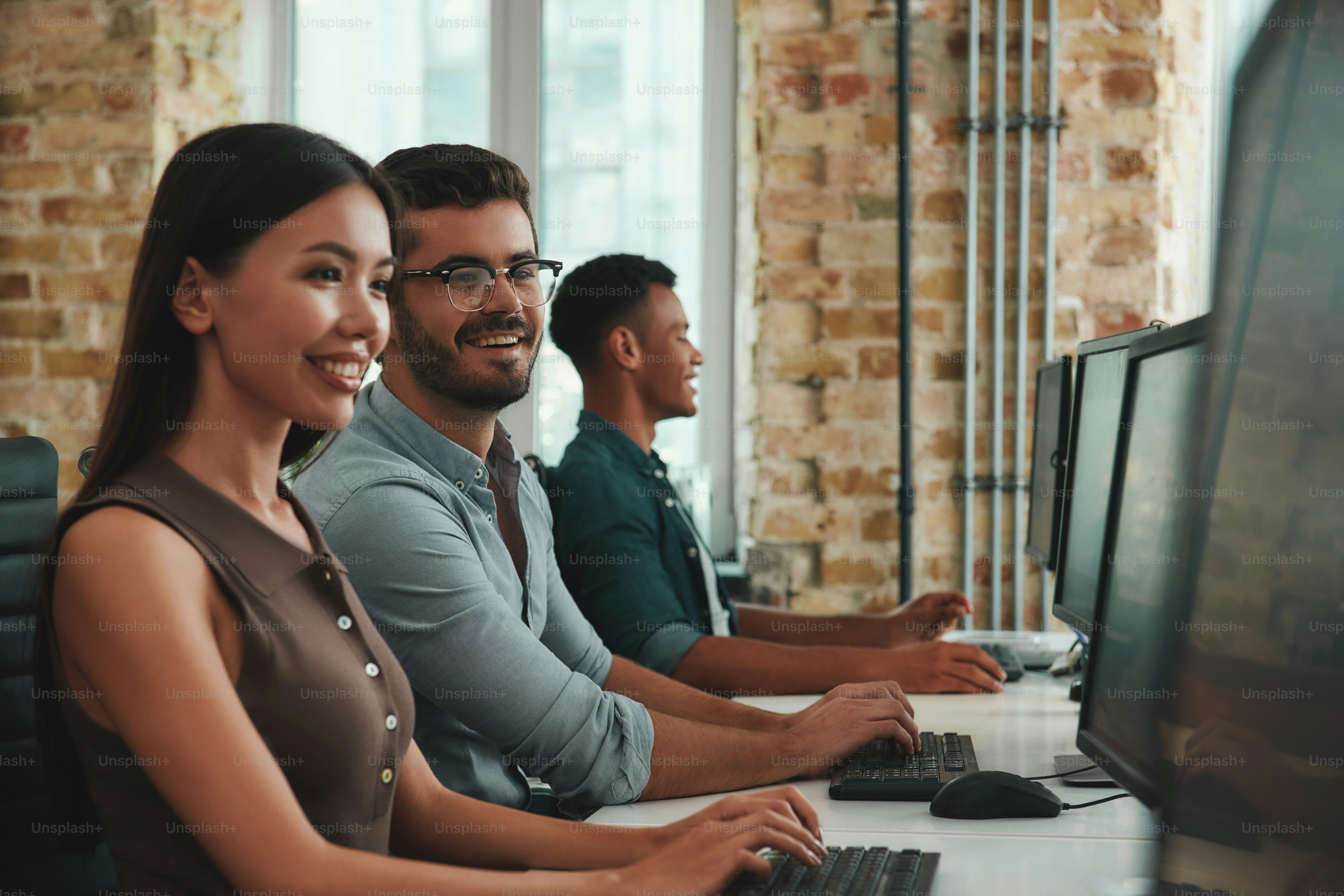 Happy to work together. Group of cheerful young employees working on computers and smiling while sitting in modern open space. Job concept. Business people. Workplace
