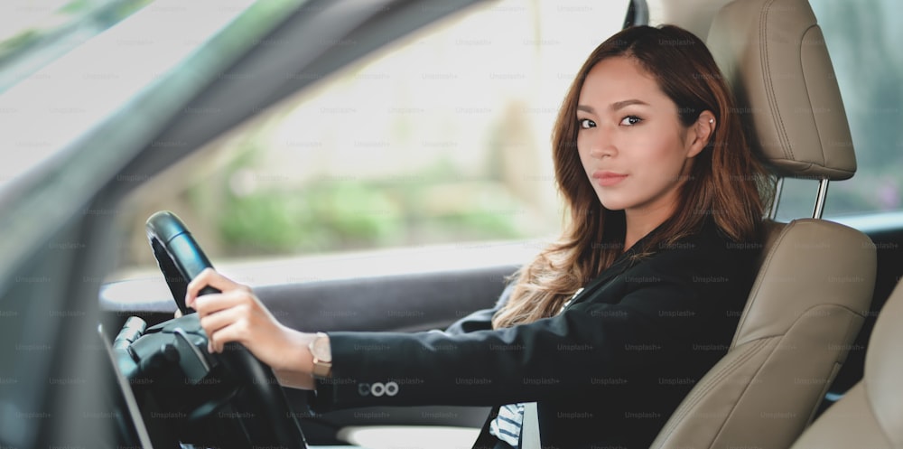 Professionelle asiatische Geschäftsfrau schaut in die Kamera, während sie mit dem Auto ins Büro fährt
