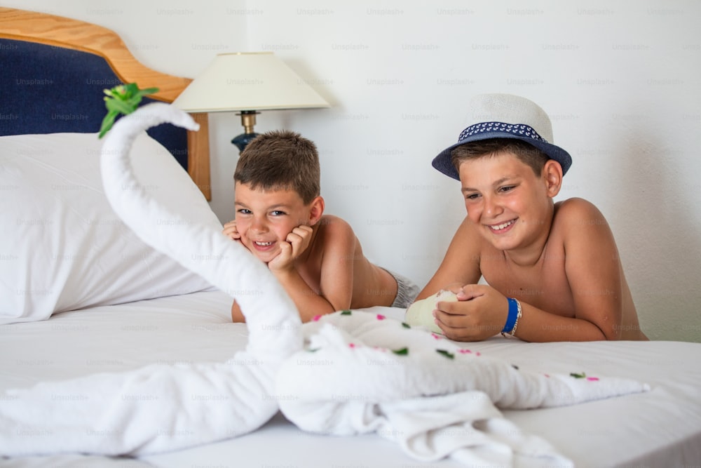 Two kids staring at beautiful swan from white bath towel decorate on bed. Happy children loving towel origami greeting from Hotel.