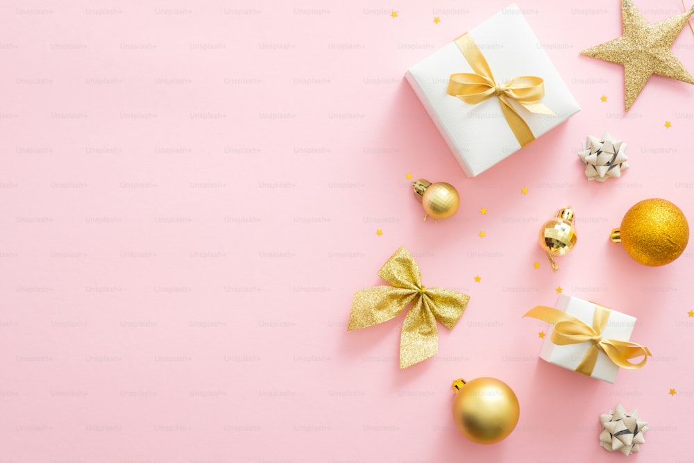 Pink Christmas background with golden decorations, gift boxes, balls, confetti, bow, star. Christmas minimal stylish composition, flat lay, top view, overhead. Christmas card mockup with copy space