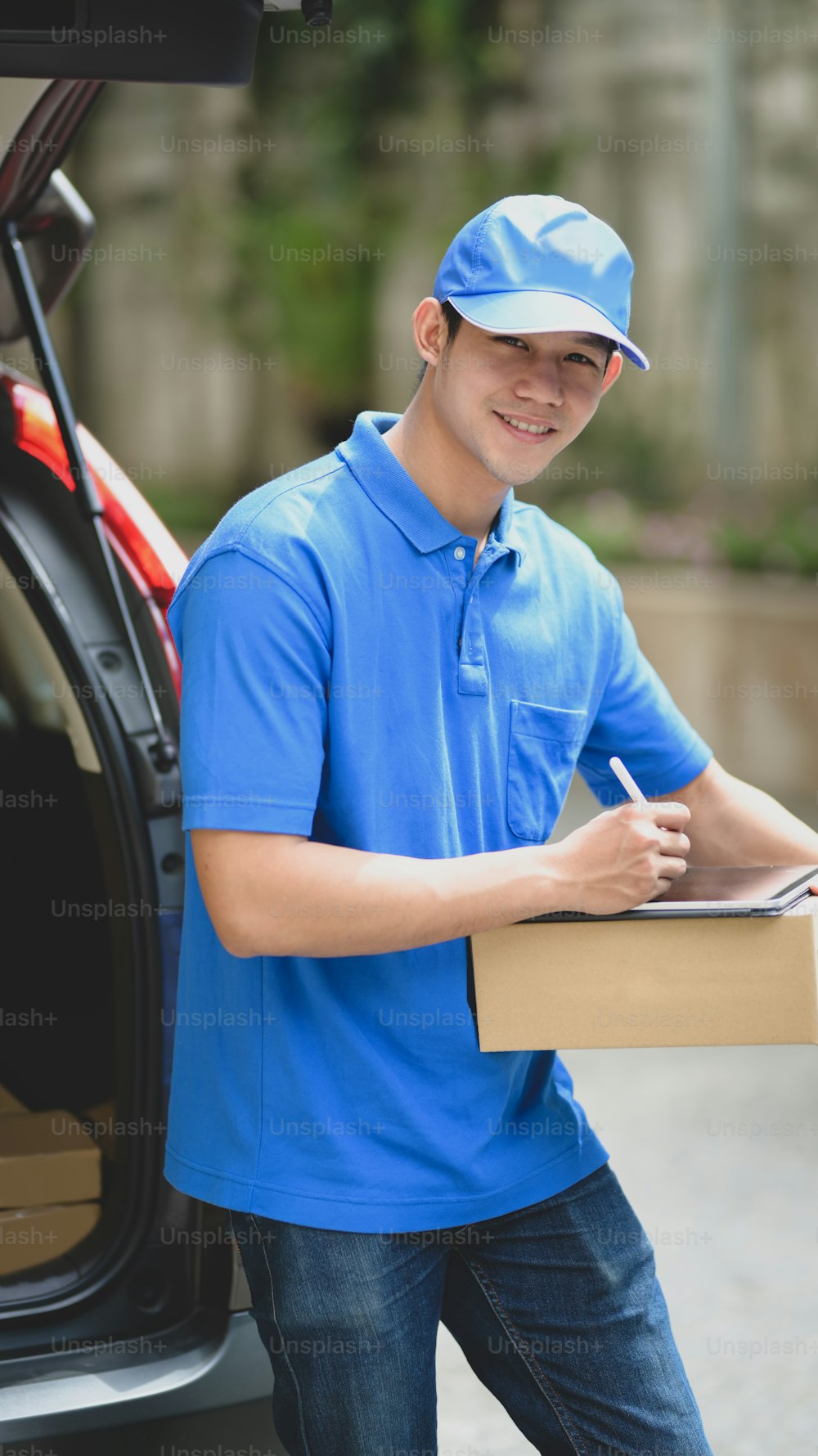Jovem entregador verificando os produtos para o cliente enquanto estava ao lado de seu carro e sorrindo para a câmera.