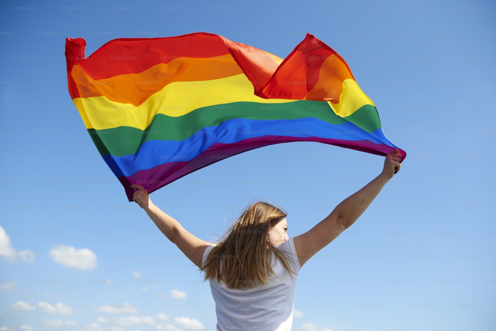 Vista posteriore della giovane donna che sventola la bandiera arcobaleno