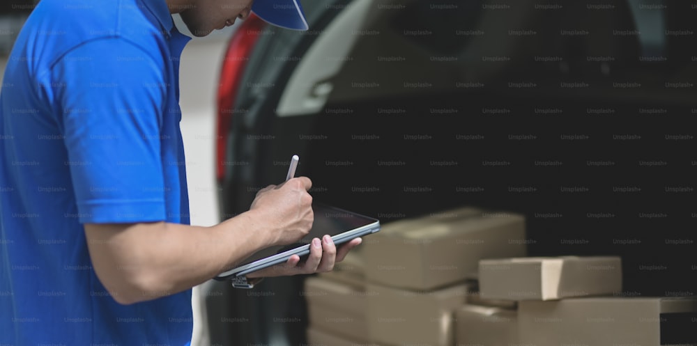 Delivery man preparing parcel box to customer while checking orders on tablet.