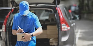Professional delivery man working with parcel boxes, customer order in the car