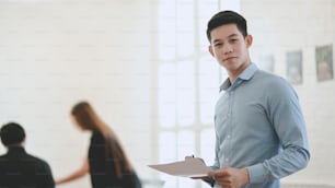 Attractive young professional businessman looking at the camera while holding document and standing in the meeting room