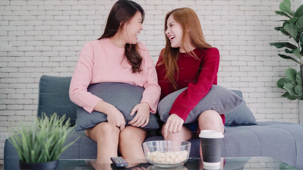 Lesbian Asian couple watching TV laugh and eating popcorn in living room at home, sweet couple enjoy funny moment while lying on the sofa when relaxed at home. Lifestyle couple relax at home concept.