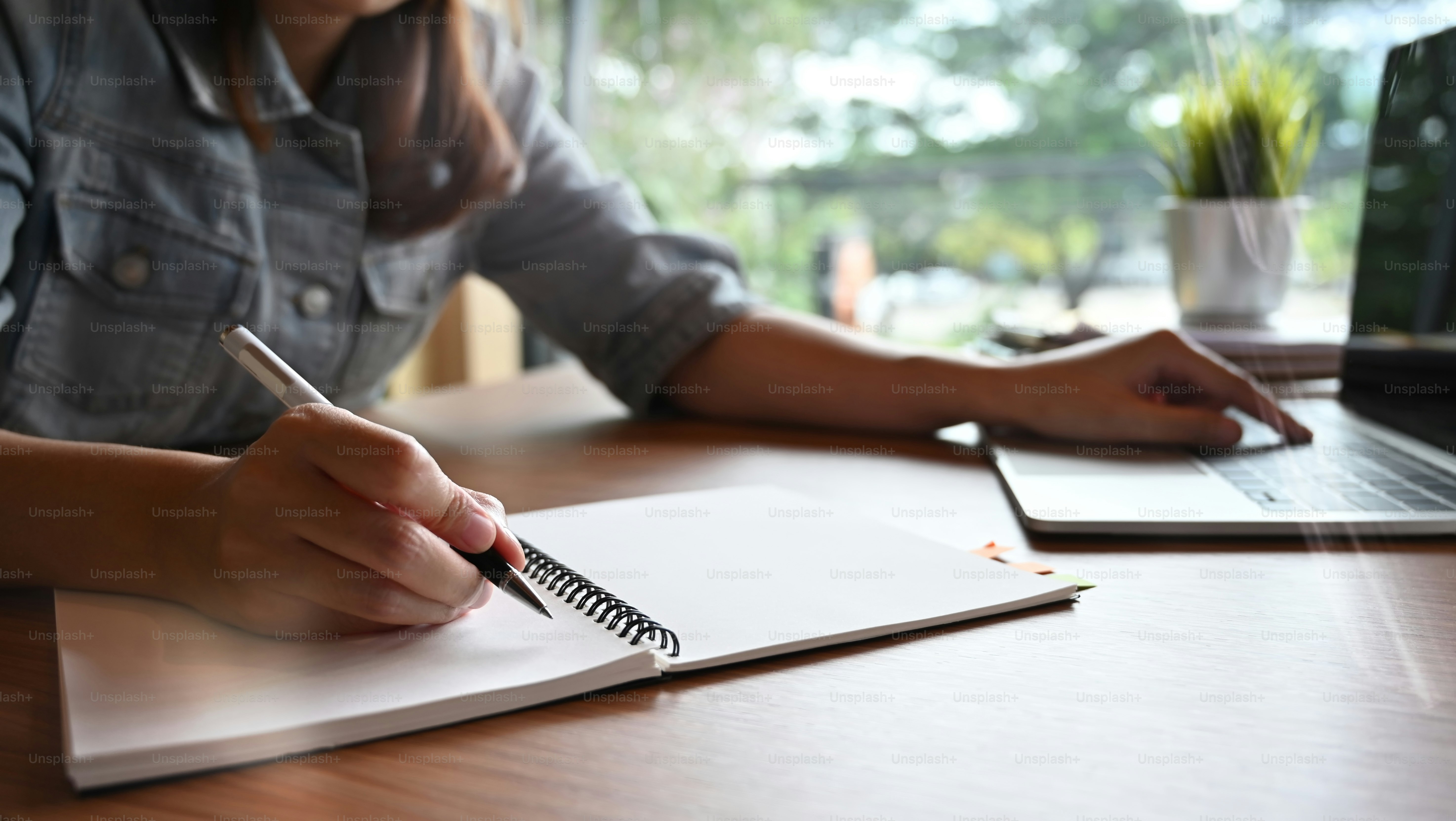 Closeup woman writing notebook and using laptop computer.