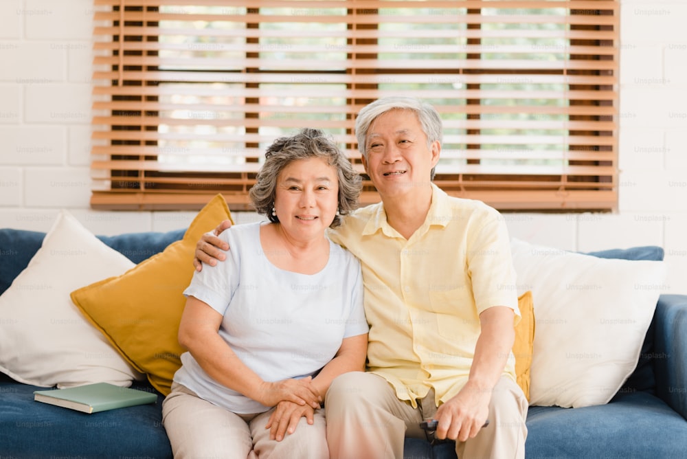 Asian elderly couple watching television in living room at home, sweet couple enjoy love moment while lying on the sofa when relaxed at home. Enjoying time lifestyle senior family at home concept.