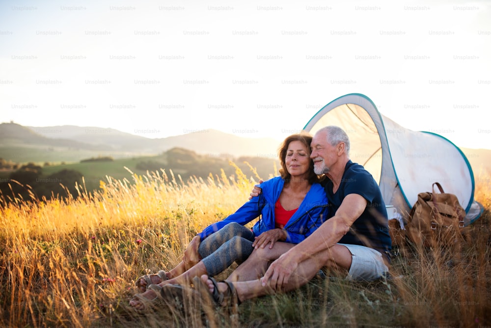 A senior tourist couple in love with shelter sitting in nature at sunset, resting.