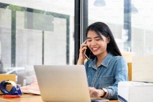 Young business startup online seller owner using computer for checking the customer orders from email or website and preparing packages for product office equipment.