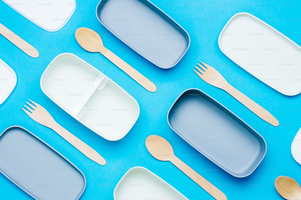 Pattern of plastic empty two-layered lunch boxes with wooden forks and spoons on blue background. Top view, flat lay.