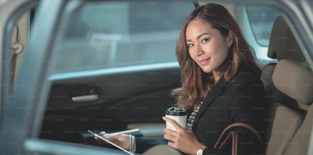 Attraente donna d'affari che lavora sull'auto con una tazza di caffè mentre si dirige verso l'ufficio