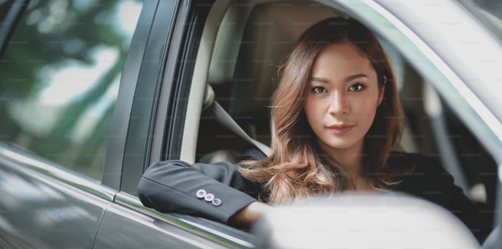 Professionelle asiatische Geschäftsfrau schaut in die Kamera, während sie mit dem Auto ins Büro fährt