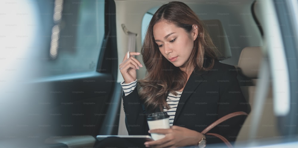 Young hard-working businesswoman working on the car with a cup of coffee while heading to the office
