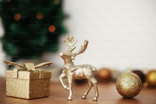Golden reindeer, gift box and glitter bauble toys on background of christmas tree with lights on rustic background. Merry Christmas and Happy Holidays. Festive decorations
