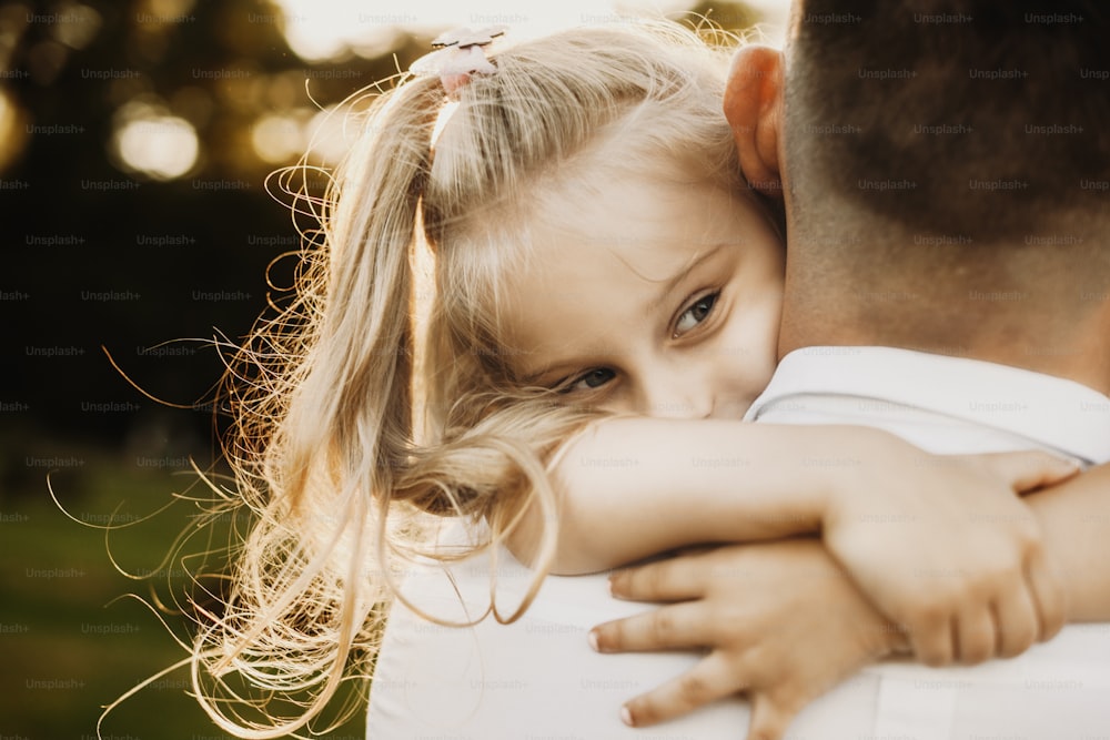 Cute small girl embracing her superhero father from neck against sunset outdoor while looking away.