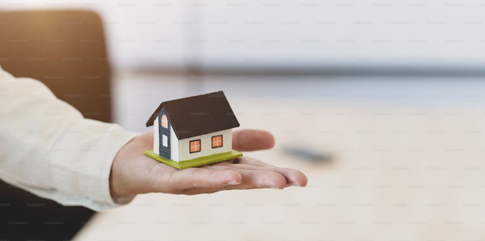 Businessman holding a house model in one hand, symbol of home insurance