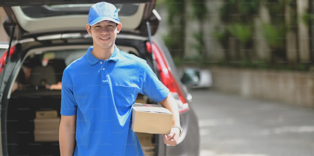 Delivery man preparing parcel box to customer and smiling to the camera while standing in front of his car