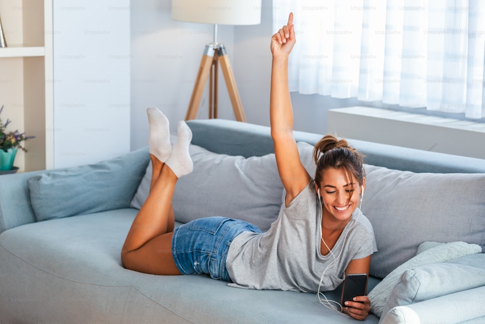 Femme ou adolescente heureuse dans des écouteurs écoutant de la musique à partir d’un smartphone et dansant sur le lit à la maison