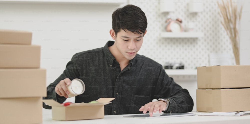 Junger männlicher Kleinunternehmer, der Bestellungen prüft und die Produkte für Kunden zu Hause vorbereitet