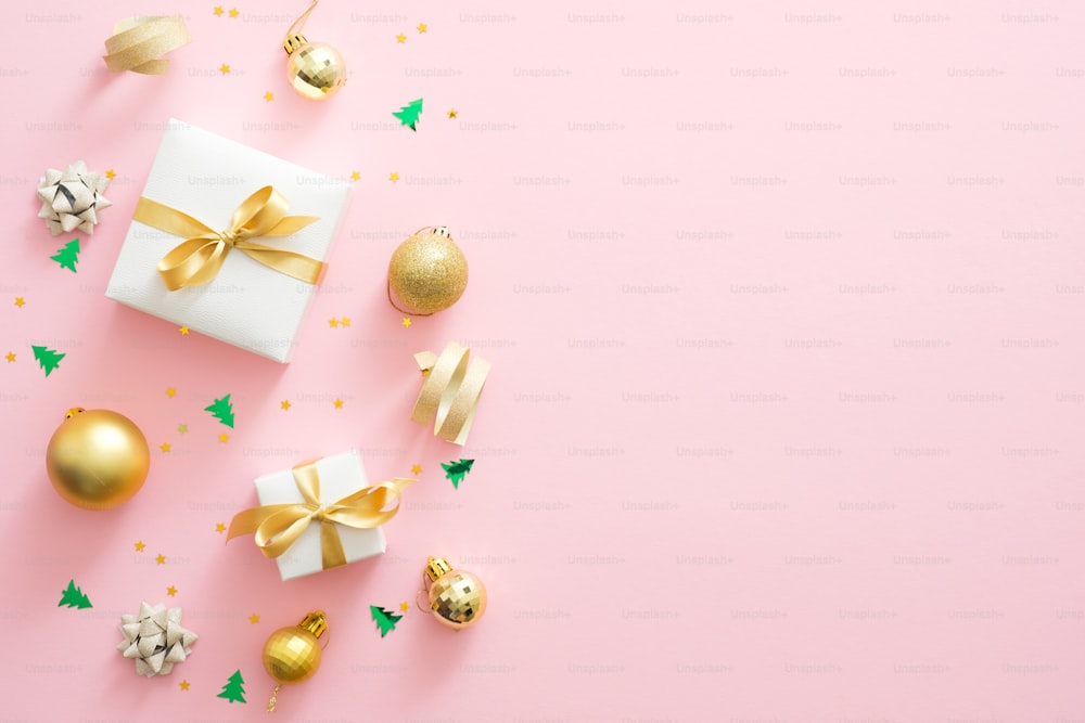 Composizione natalizia. Decorazioni natalizie dorate, scatole regalo, palline, coriandoli su sfondo rosa pastello con spazio di copia. Posa piatta, vista dall'alto