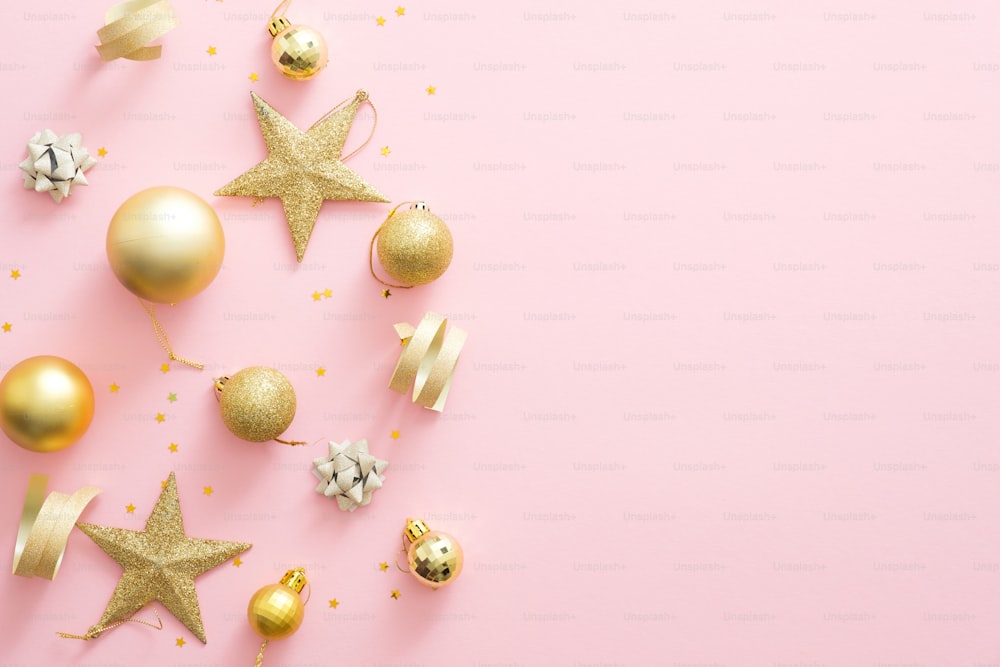 Christmas golden decorations on pastel pink background with copy space. Glitter baubles, stars, confetti. Flat lay, top view. Christmas, winter holidays, New Year concept