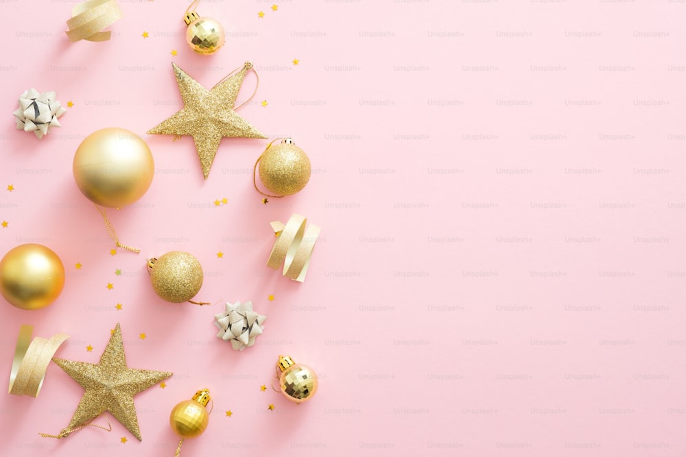 Christmas golden decorations on pastel pink background with copy space. Glitter baubles, stars, confetti. Flat lay, top view. Christmas, winter holidays, New Year concept