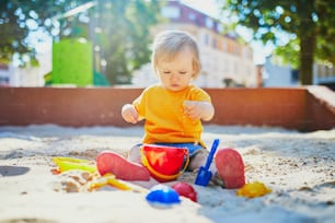 모래 구덩이의 놀이터에서 즐거운 시간을 보내는 사랑스러운 어린 소녀. 모래 곰팡이를 가지고 놀고 진흙 파이를 만드는 유아. 아이들을 위한 야외 창작 활동