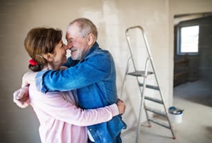 Portrait of cheerful senior couple painting walls in new home, hugging. Relocation concept.