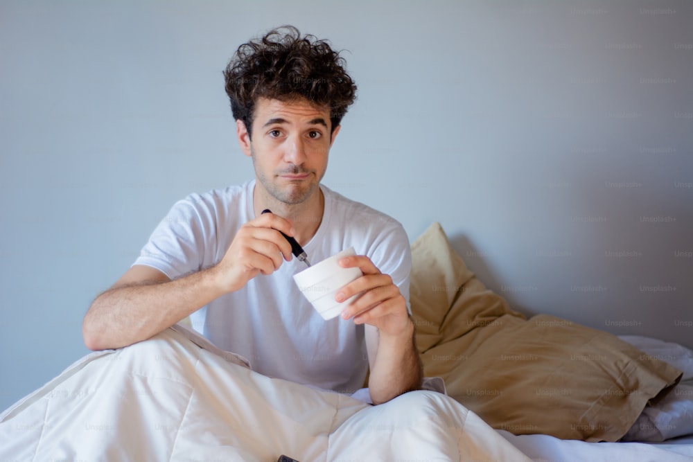 Jeune homme mangeant de la crème glacée tout en se reposant dans le lit à la maison. Dedans