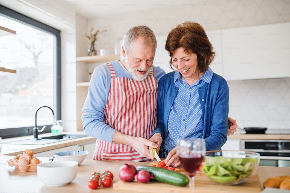 Un retrato de una pareja de ancianos felices enamorados en el interior de la casa, cocinando.