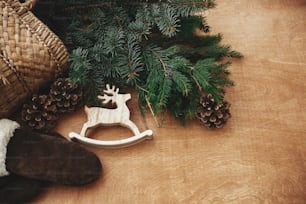 Zero waste Christmas. Rustic reindeer toy, gloves, basket with fir branches and cones on rustic wooden background. Winter holiday preparations. Slow living. Seasons greeting. Copy space.
