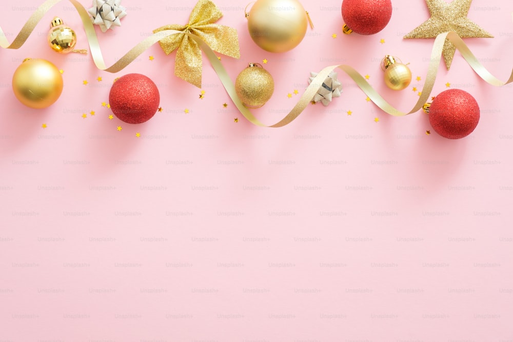 Christmas holiday composition. Christmas tree fir branches, colorful balls, golden ribbon on top border on pastel pink background. Banner mockup, postcard template. Flat lay, top view, overhead.