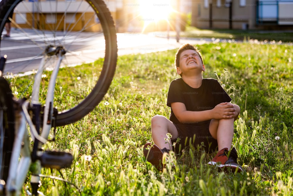 Niño en el suelo de la calle con una lesión en la rodilla gritando después de caerse de su bicicleta. Un niño se lastima la pierna después de caerse de su bicicleta