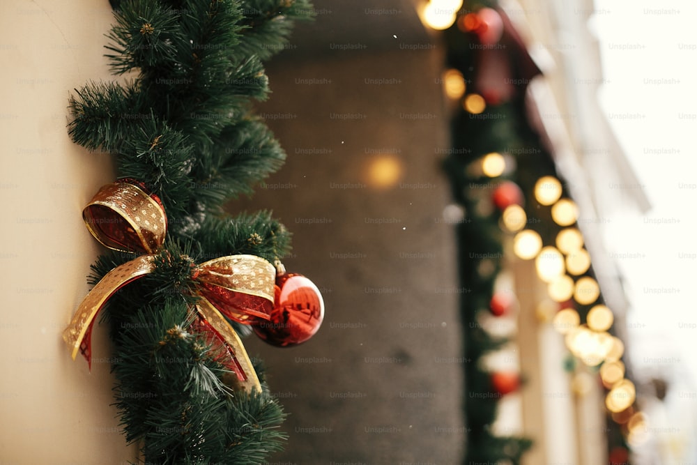 Weihnachtliche Straßendekoration. Stilvolle Weihnachtstannenzweige mit goldenen Lichtern, roten festlichen Kugeln und Schleife auf Schaufensterladen auf dem Weihnachtsmarkt in der Stadtstraße. Platz für Text.