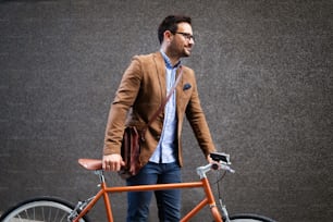 Young stylish businessman going to work by bike in the city
