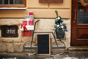 Christmas street decor. Stylish bicycle with christmas gifts and modern christmas tree at store front at holiday market in city street. Wooden board with space for text