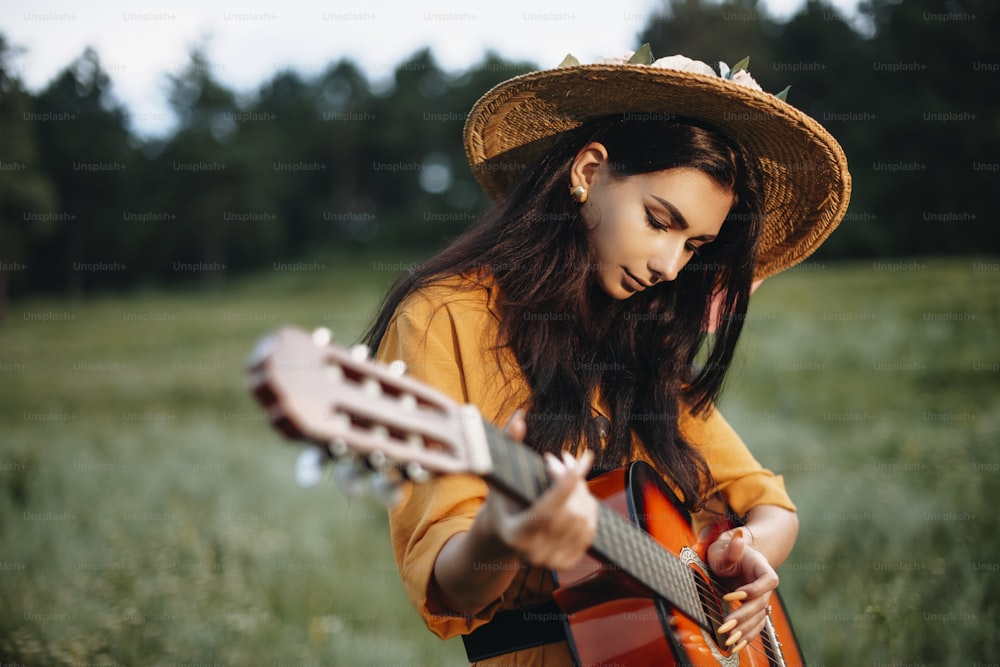 Toma al aire libre de una encantadora joven tocando una guitarra en la naturaleza.