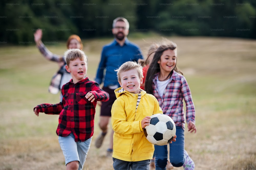 Um grupo de crianças pequenas em idade escolar com professor em viagem de campo na natureza, brincando com uma bola.